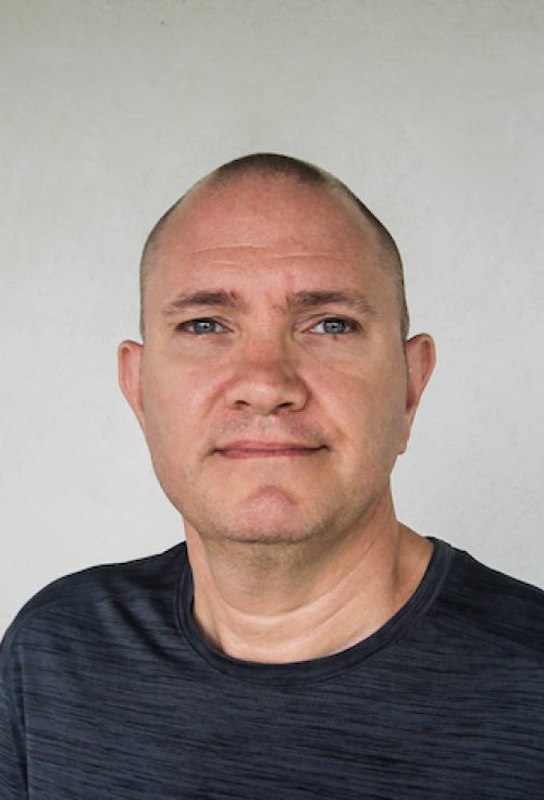 Headshot of a man with a shaved head wearing a dark blue shirt against a plain light background