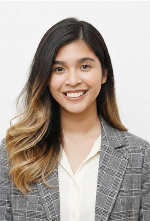 Portrait of Janine Mayo smiling, wearing a grey checked blazer and white blouse, against a plain white background
