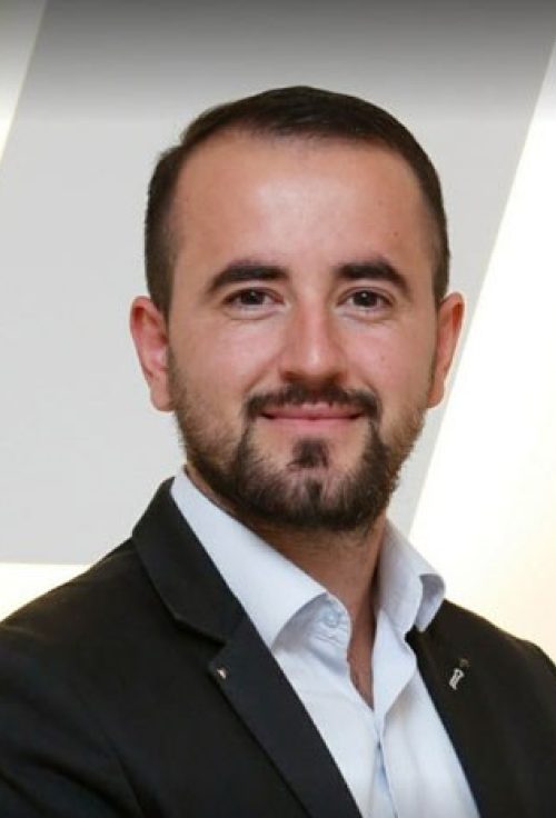 Portrait of a man with short dark hair and beard wearing a suit jacket and white shirt