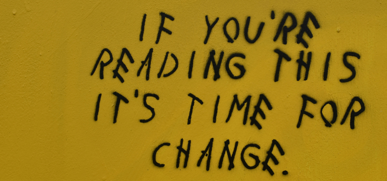 Black graffiti text reading 'If you're reading this it's time for change' on a yellow painted wall