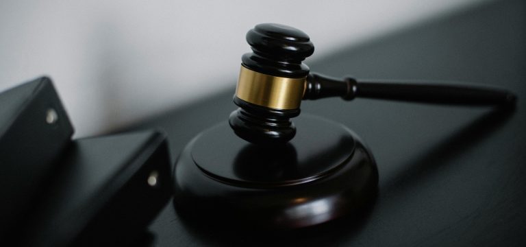 Close-up of a judge's gavel resting on a desk with black binders in the background, symbolising legal proceedings and expert witness services