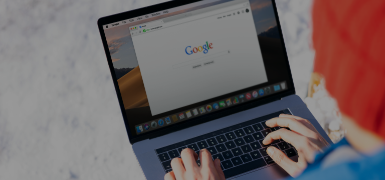Hands typing on a MacBook keyboard showing the Google search homepage on screen