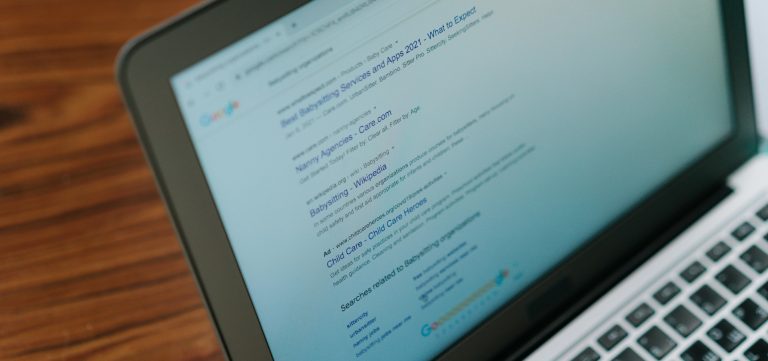 Laptop screen showing Google search results page with listings for babysitting services and related search suggestions