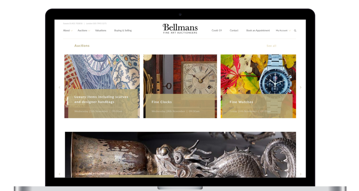 Laptop screen displaying the Bellmans auctioneers website homepage featuring luxury items, fine clocks and fine watches auctions