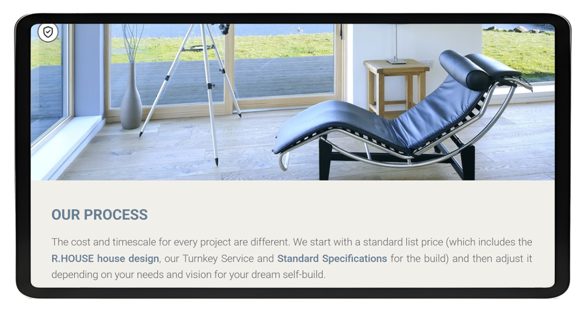 Tablet screen showing the Rural House website featuring a modern interior with a black leather lounge chair and large windows overlooking a green landscape