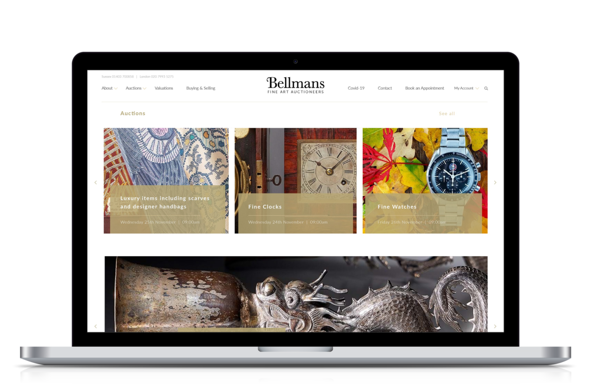 Laptop screen displaying the Bellmans auctioneers website homepage featuring luxury items, fine clocks and fine watches auctions