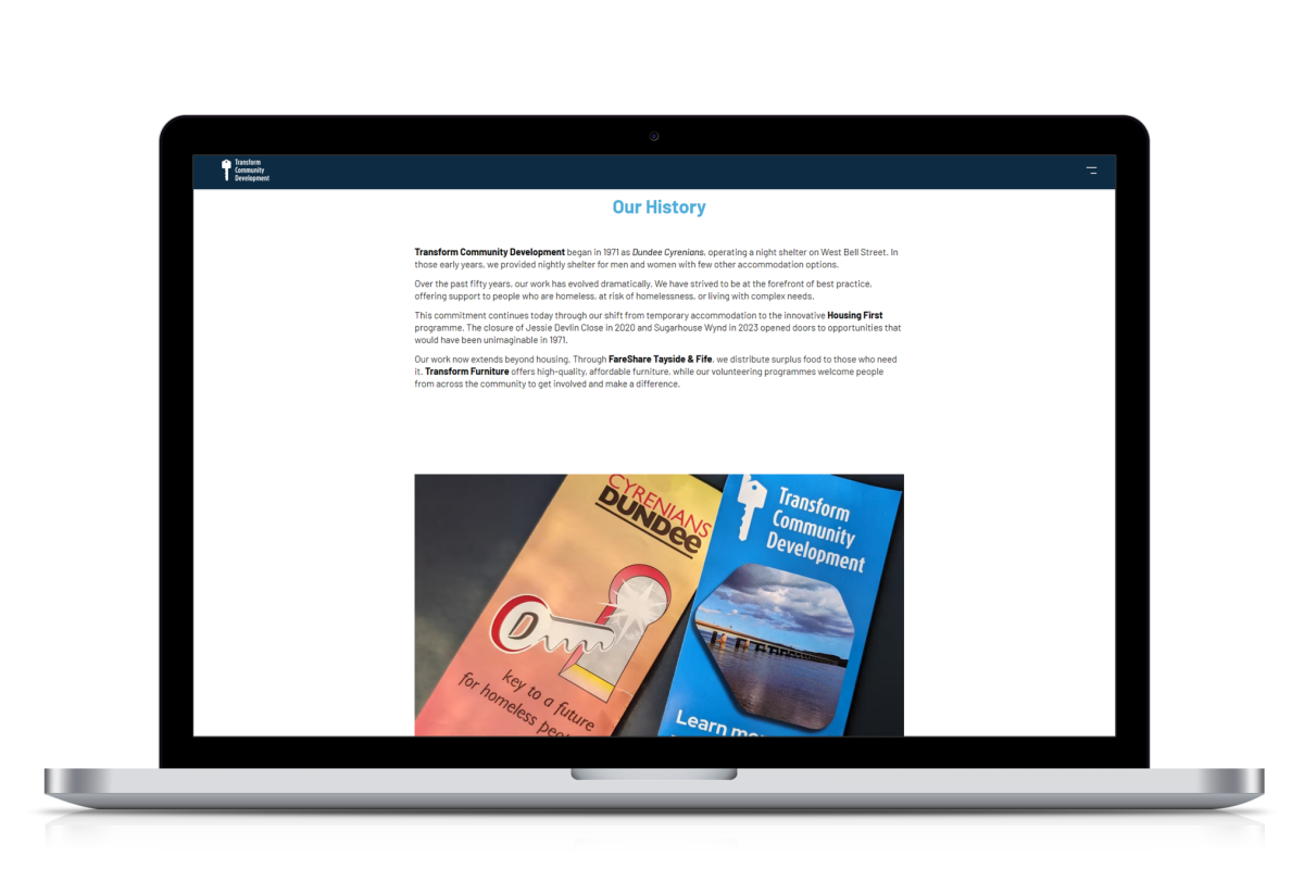 Laptop screen displaying the 'Our History' page of the Transform Community Development website with text about the organisation's origins and two brochures showing the organisation's branding.