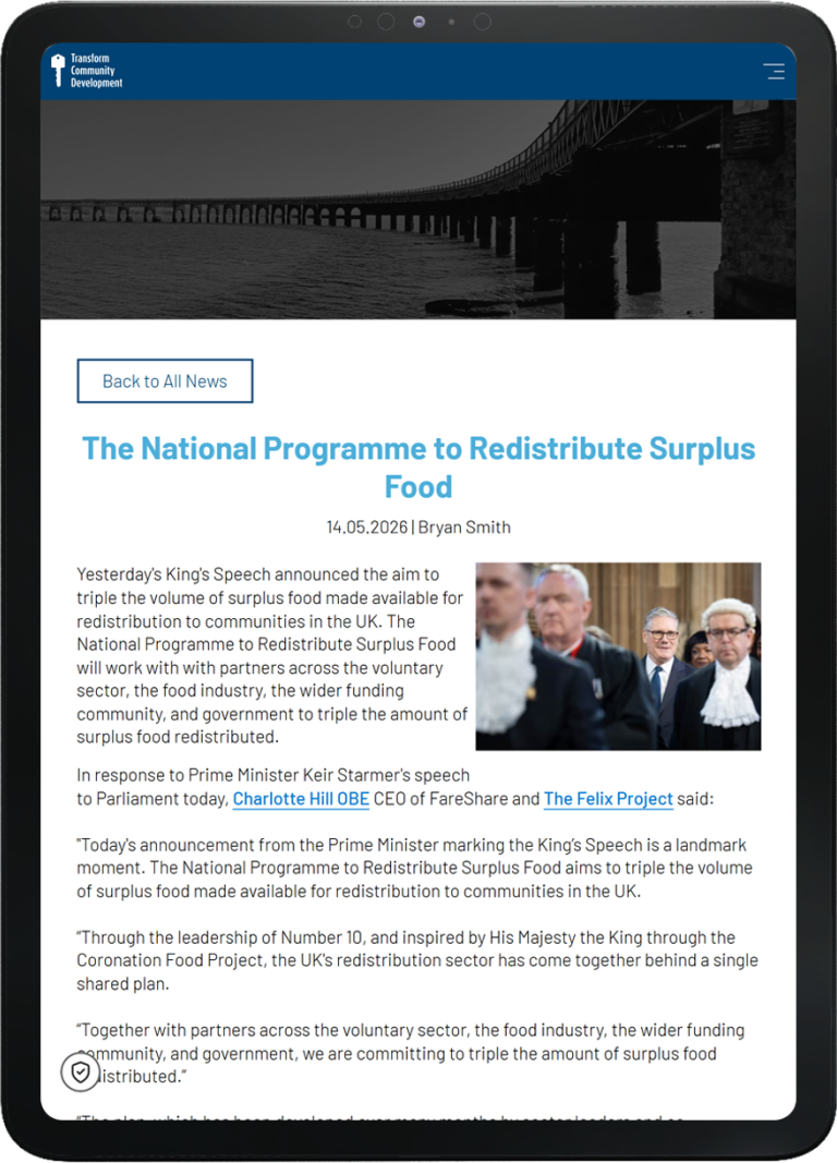 Tablet showing the Transform Community Development website with a banner image of a long bridge and navigation menu